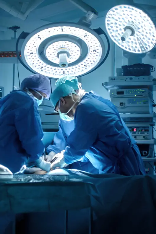 Two doctors performing an emergency operation in an operating room, with a blue color theme. In the background, there is equipment and lights. The patient is lying on their back on the operating table under a neon light. Both doctors are wearing surgical caps.
