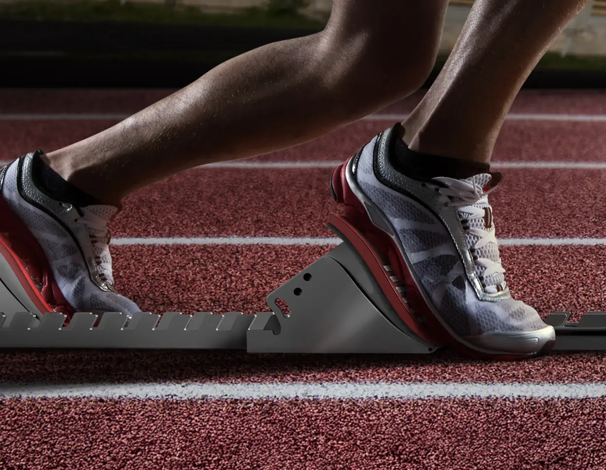 Close-up of an athlete’s feet on the starting blocks, ready to start in a track and field competition. The shoes have a gray gradient color with red details, standing at attention near the start line on the stadium track surface. Bright daylight illuminates them, highlighting their powerful stance against a vibrant background.