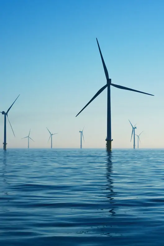A photograph of wind turbines in the ocean, with clear blue skies above and calm waters below. The scene captures an eco-friendly energy plant at sea, showcasing sustainable power generation through renewable energy sources. This shot is perfect for conveying concepts of environmental sustainability or green technology.